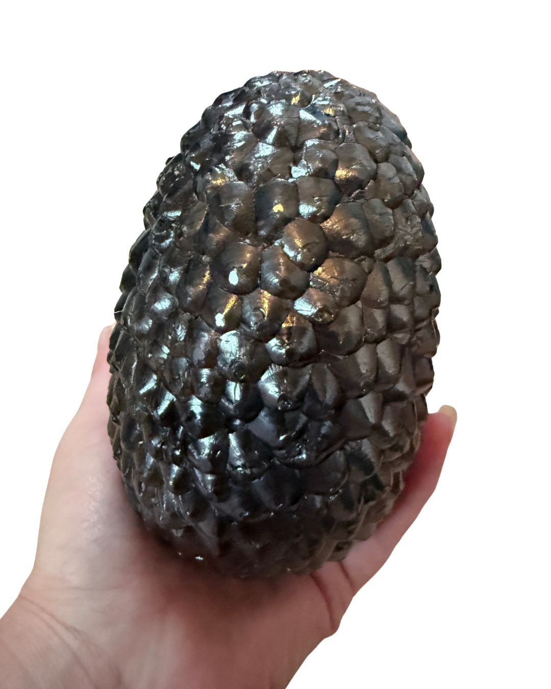 A hand holding a large, textured dark gray stone replica of a pinecone against a plain white background.